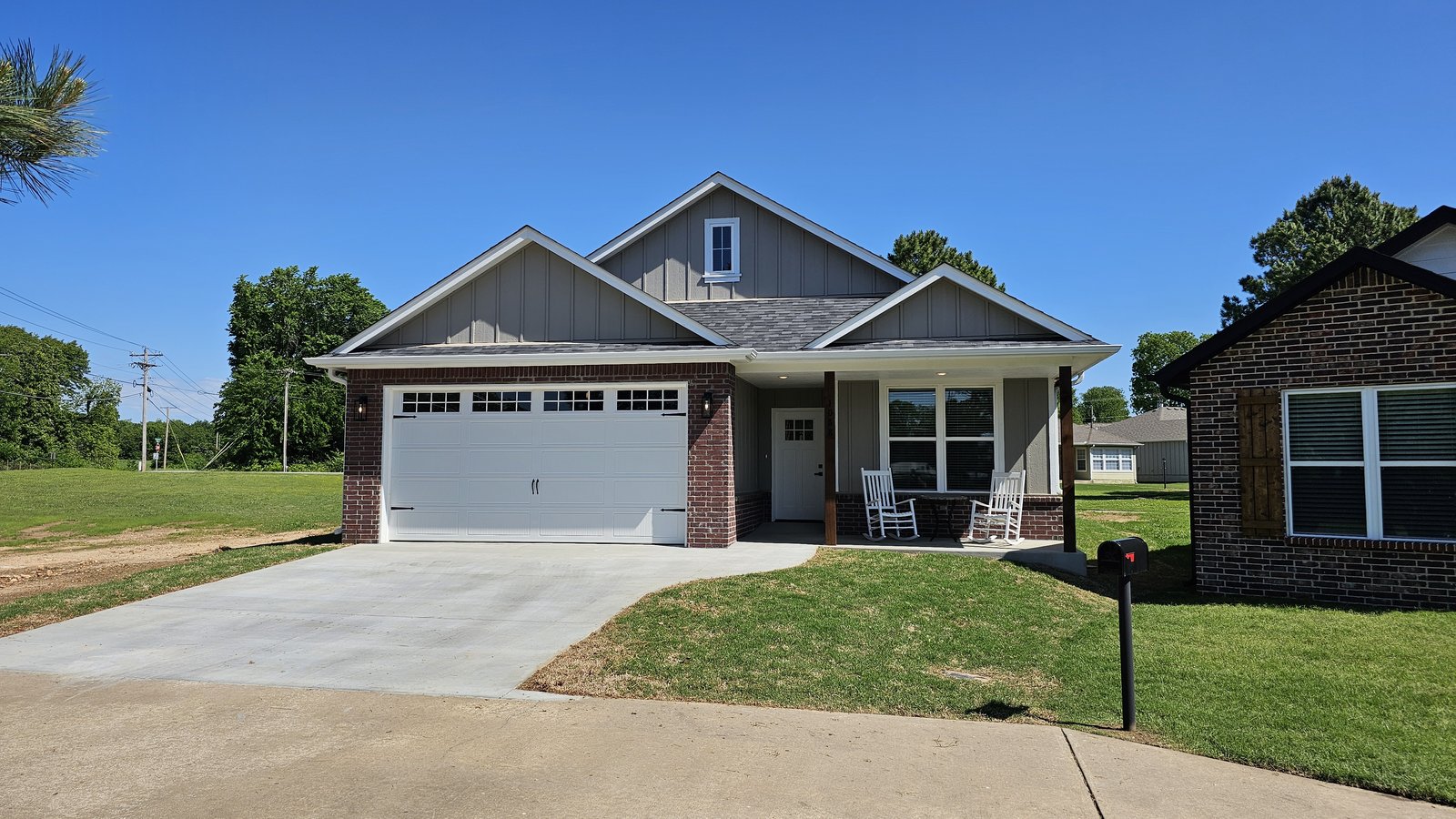 Front elevation of gray siding and brick custom home with white garage door on a sloped lot
